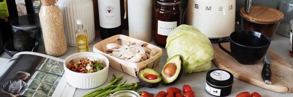 Assorted healthy food and vegetables set locating on gray countertop next to various utensils and appliances during cooking in stylish kitchen
